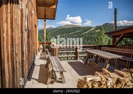 Casa di campagna tradizionale nelle Alpi. Estate con cielo blu e prato verde. Terrazza in legno con tronchi di legno intemperiato. Casa sulla cima della montagna. Noleggio a h Foto Stock