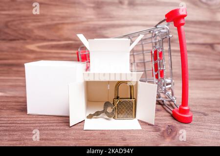 Carrello rovesciato con scatole di consegna, lucchetto in bronzo e chiave su un tavolo in legno. Foto Stock