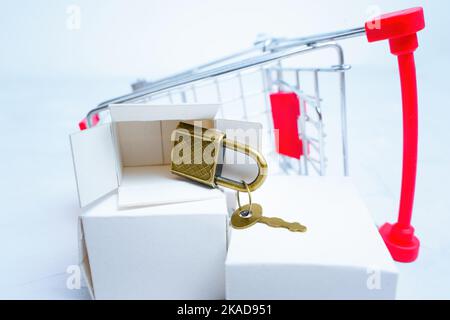 Piccolo lucchetto in bronzo con chiave che cade da una scatola di consegna bianca posta da un carrello a spinta miniaturizzato rovesciato. Concetto di negozio hardware di sicurezza. Foto Stock