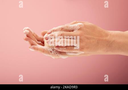 Un primo piano di mani femminili che insaporiscono le mani con un pezzo di sapone schiumoso su sfondo rosa Foto Stock