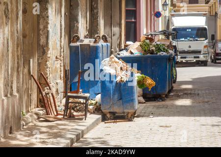 Traboccante pattumiera urbana da edifici rovinosi e rovinosi. Alcuni mobili sono sul marciapiede. La strada è fatta di ciottoli Foto Stock