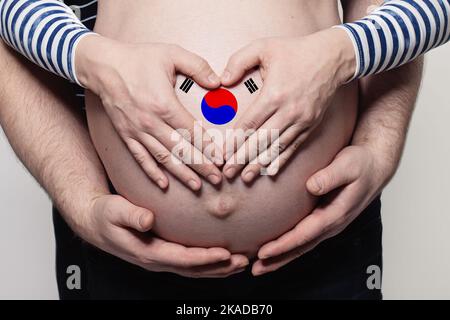 Concetto familiare coreano. Uomo che abbraccia il ventre e il cuore di donna incinta con bandiera della Repubblica di Corea colori primo piano Foto Stock