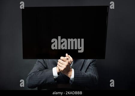 Uomo d'affari in abiti con TV invece della testa sul nero Foto Stock