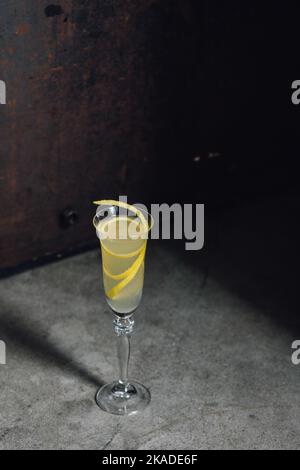 cocktail francese di champagne 75 con tocco limone guarnire in flauto vetro contro cemento rustico metallo Foto Stock