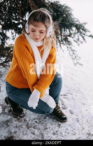 Teen bionda in un maglione giallo fuori in inverno. Una ragazza adolescente in una passeggiata in abiti invernali in una foresta innevata. Foto Stock