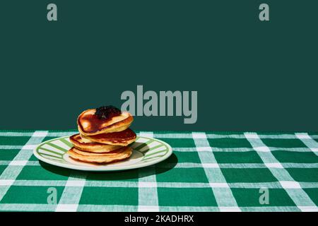 Piatto di deliziosi pancake dolci con marmellata su tovaglia verde su sfondo verde Foto Stock