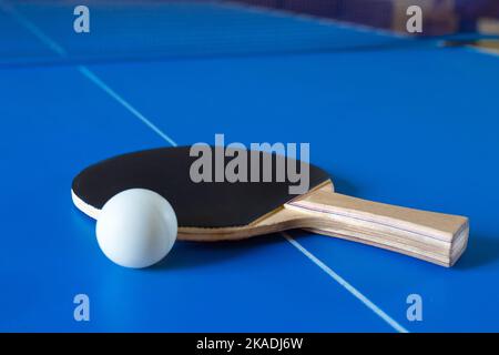 Racchetta di legno per ping pong e palla bianca sdraiata sul tavolo blu Foto Stock