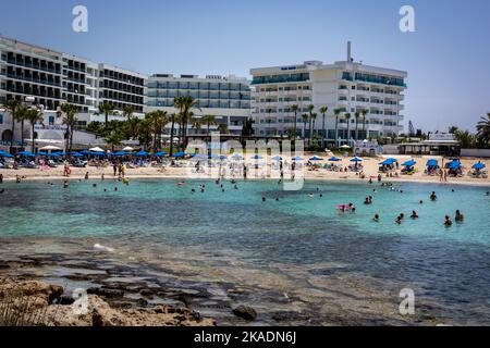 Ayia Napa, Cipro - 24 giugno 2022: Spiaggia di Viathia Gonia. Persone che fanno il bagno in mare, edifici di hotel sullo sfondo. Foto Stock