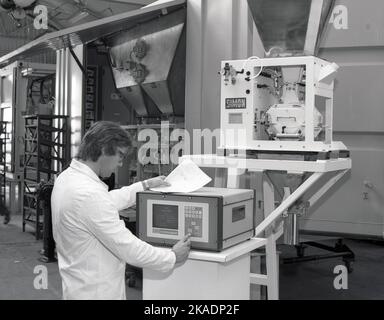 1980s, storico, tecnico maschile che aziona il computer di una macchina su una macchina riempitrice di fertilser, fatta da Richard Simon & Sons, di Nottingham, Inghilterra, UK. Schermo sulla macchina dice Simon Computapak, con menu che dà opzioni compreso il peso Foto Stock