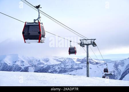 Funivia presso la stazione sciistica con montagne innevate sullo sfondo. Moderno skilift con funitelle e torri di sostegno in alto sulle montagne Foto Stock
