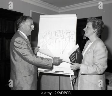 1980s, storico, all'interno di una sala conferenze dell'hotel, un presentatore maschile adatto, in piedi con una collega femminile, accanto a una lavagna con la parola 'Change', scritta sul consiglio di amministrazione. La signora ha in mano un opuscolo intitolato "l'eccellenza attraverso la qualità". In quest'epoca, le lavagne sono state utilizzate nelle presentazioni come ausilio visivo e hanno avuto il vantaggio di aggiungere un elemento di interattività a una presentazione, in quanto parole e commenti possono essere facilmente aggiunti o toluti durante la sessione. Foto Stock