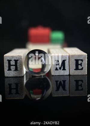 La parola casa è isolata in uno sfondo scuro. Case di plastica rosse e verdi. La parola casa è scritta su cubi di legno. Una sfera di vetro o una sfera con Foto Stock