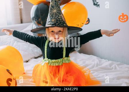 Halloween per bambini - una ragazza in un cappello da strega e un costume da  carnevale con palloncini arancioni e neri a casa. Pronto a festeggiare  Halloween Foto stock - Alamy