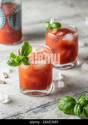 Succo di pomodoro o cocktail ghiacciato Bloody Mary con foglie di bazil in due bicchieri e bottiglia per menu bevande Foto Stock