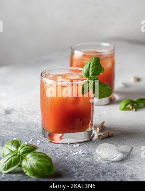 Succo di pomodoro o cocktail ghiacciato Bloody Mary con foglie di bazil in due bicchieri per un menu di bevande con spazio di testo Foto Stock