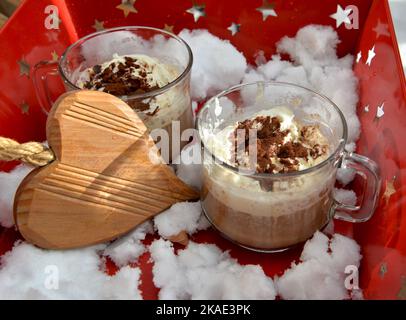 tazze di cappuccino e cuore di legno poste in un vassoio rosso con la neve Foto Stock