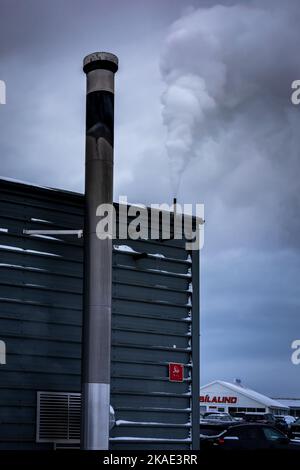 Reykjavik, Islanda - 25 gennaio 2022: Un camino grigio su un edificio di lavanderia, fumo di vapore che esce. Grigio giorno d'inverno. Foto Stock