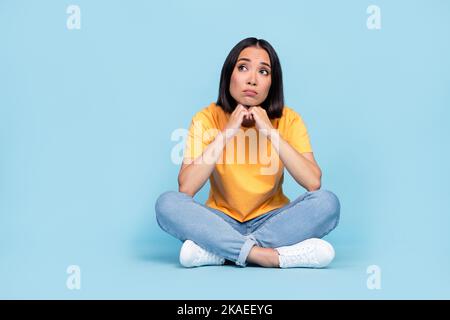 Foto del corpo di bella giovane ragazza cinese seduto pavimento triste psicoterapia vestita elegante giallo sguardo isolato su sfondo di colore blu Foto Stock