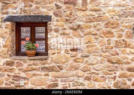 Il pittoresco muro esterno di casa in pietra con fiori nel villaggio di Barcena Mayor in Spagna Foto Stock