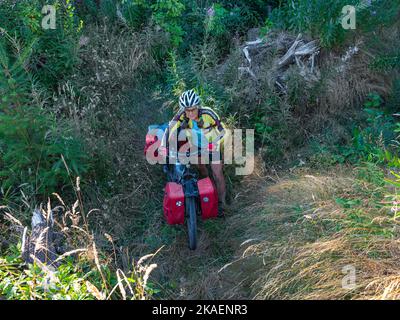 WA22674-00...WASHINGTON - spingendo la sua bici attraverso una sezione stretta e molto brushy del percorso lungo il bordo di un taglio netto vicino al lago di Sandy Shore. Foto Stock