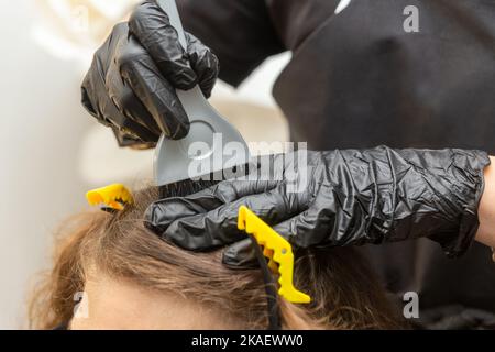 Ragazza in gomma nera guanti protettivi tenendo una spazzola nelle sue mani e mescolando tintura capelli primo piano. Cura dei capelli del colorista alla maschera dei capelli del salone di bellezza. Foto Stock