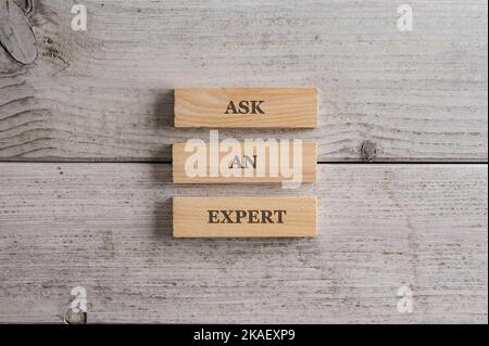 Chiedi un cartello esperto scritto su tre picchetti di legno impilati posti su uno sfondo di legno bianco. Foto Stock