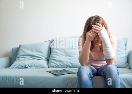 Una donna con un gesso sul braccio tiene la testa. Depressione, disperazione, collasso dei piani. Donna in depressione. Foto Stock