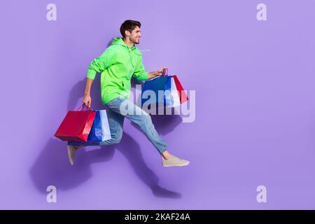 Foto a tutta lunghezza di un uomo eccentrico eccitato indossare verde in attesa di affari jumping alto vuoto spazio isolato colore viola sfondo Foto Stock