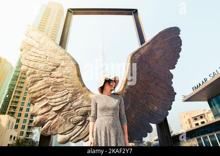 Dubai, Emirati Arabi Uniti - 12th ottobre 2022: Posa turistica caucasica femminile delle ali del Messico scultura moderna di Jorge Marin e Burj Khalifa edificio nel Foto Stock