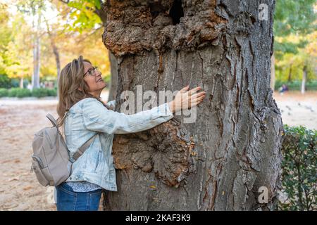 Donna che abbraccia il tronco di un grande albero di grande antichità pieno di solchi nel corso degli anni. Foto Stock