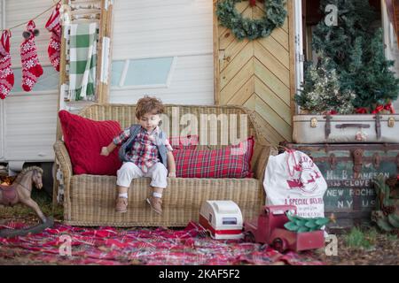 Un bambino bianco seduto su un divano di fronte a un furgone bianco con decorazioni natalizie e di Capodanno Foto Stock