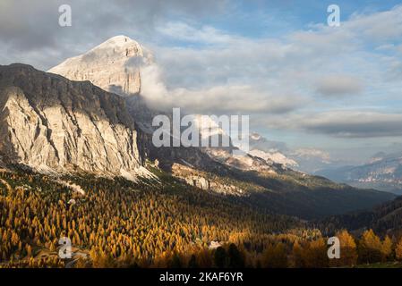 Le nuvole circondano la faccia sud delle Tofane di Rozes sopra le foreste montane autunnali sul Passo Falzarego al sole serale, Dolomiti, Italia Foto Stock