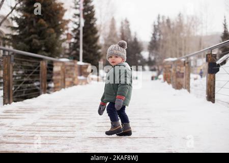 Un bambino che indossa un beanie C.C che cammina su un ponte innevato Foto Stock