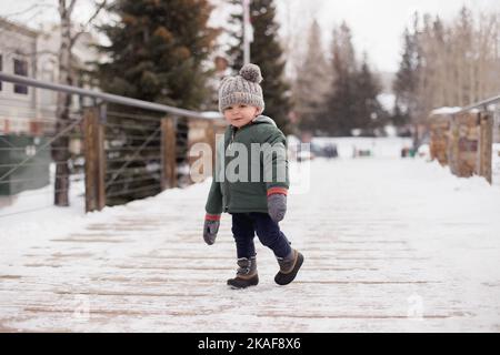 Un bambino bianco che cammina su un ponte innevato indossando un beanie C.C. Foto Stock