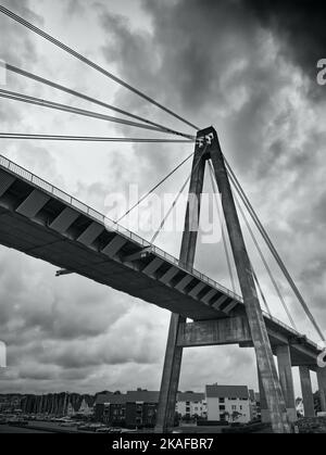 Una scala di grigi verticale di un ponte sospeso sotto il cielo nuvoloso Foto Stock