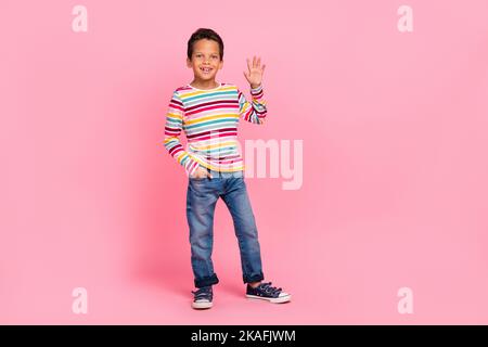 Foto a tutta lunghezza di positivo dolce ottimista ragazzo vestito camicia a righe jeans braccio in tasca onda palma isolato su sfondo di colore rosa Foto Stock