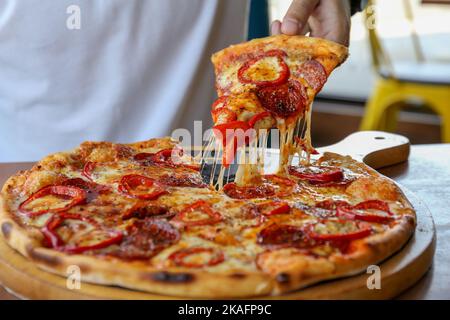 Lo chef sta prendendo una fetta di pizza appena sfornata, primo piano Foto Stock