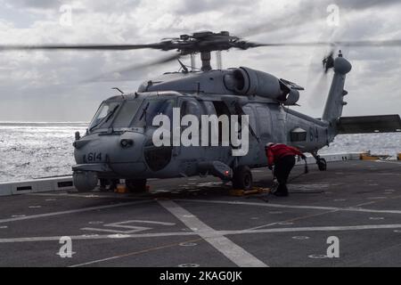 221026-N-XB010-1008 East China Sea (ott 26, 2022) – i marinai assegnati alla nave portuale di trasporto anfibio USS New Orleans (LPD 18) rimuovono i cunei e le catene da un elicottero MH-60R/S Sea Hawk assegnato all'elicottero Sea Combat Squadron (HSC) 12 Golden Falcons dalla superportatrice nucleare USS Ronald Reagan (CVN 76) Nel Mar Cinese Orientale. New Orleans, parte della Ronald Reagan Amphibious Strike Force, opera nell'area di responsabilità della flotta statunitense 7th per migliorare l'interoperabilità con alleati e partner e servire come pronta risposta f Foto Stock