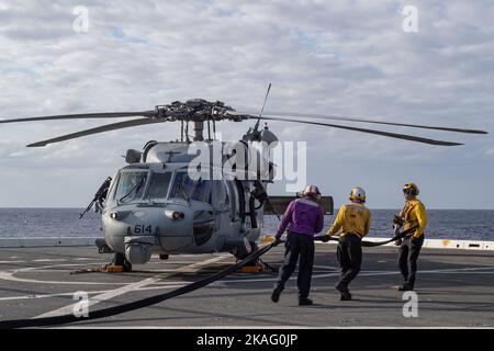 221026-N-XB010-1012 East China Sea (ott 26, 2022) – i marinai assegnati alla nave portuale di trasporto anfibio USS New Orleans (LPD 18) trasportano una linea di alimentazione ad un elicottero MH-60R/S Sea Hawk assegnato all'elicottero Sea Combat Squadron (HSC) 12 Golden Falcons dalla superportatrice nucleare USS Ronald Reagan (CVN 76) Per rifornire mentre si trova nel Mar Cinese Orientale. New Orleans, parte della Ronald Reagan Amphibious Strike Force, opera nell'area di responsabilità della flotta statunitense 7th per migliorare l'interoperabilità con alleati e partner e servire come pronto riposo Foto Stock