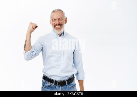 Entusiasta uomo anziano, uomo d'affari che alza il pugno clenched, vincendo o trionfando, in piedi su sfondo bianco Foto Stock