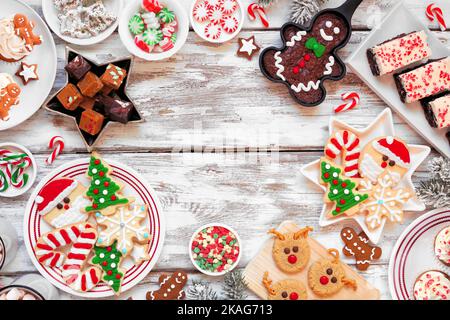 Dolci di Natale carino e cornice cookie. Vista dall'alto su uno sfondo rustico di legno bianco con spazio copia. Concetto di cottura di festa di divertimento. Foto Stock