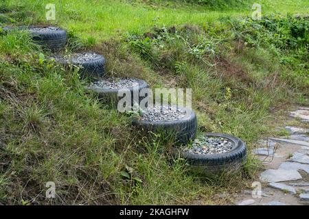 Vecchia auto usata pneumatici riempiti di pietre di granito roccia per fare scale sul pendio in cortile. Upcycling degli pneumatici di riutilizzo. Foto Stock