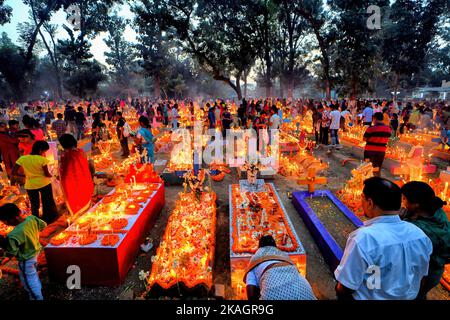 I membri della famiglia cristiana pagano rispetto e offrono preghiere accanto alle tombe dei loro parenti durante la Giornata delle ANIME. I devoti cristiani si riuniscono nelle tombe dei loro cari in un cimitero con candele e fiori accesi durante la Giornata delle ANIME. Un giorno in cui i cristiani ricordano i loro amici e parenti, che sono passati via. Ciò deriva da un'antica credenza che le anime dei morti ritorneranno, in questo giorno particolare, per consumare un pasto con la loro famiglia & amici. Le candele sono accese per guidare le anime a casa loro per il pasto. Foto Stock