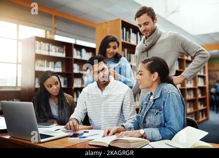 Tutti abbiamo bisogno di qualche spiegazione di tanto in tanto: Un gruppo di studenti universitari che studiano in biblioteca. Foto Stock