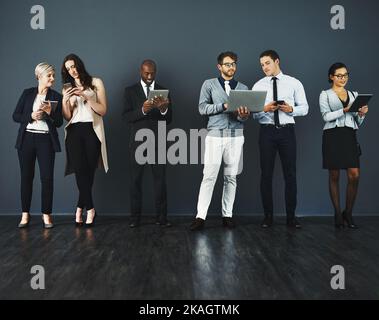 Theyve tutti hanno ottenuto i sensi astuti fare il commercio. Studio di un gruppo di uomini d'affari che utilizzano vari dispositivi digitali su uno sfondo grigio. Foto Stock