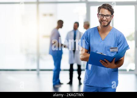 Preparazione alla dimissione del paziente. Ritratto di un giovane medico che legge il contenuto di un file con i suoi colleghi sullo sfondo. Foto Stock