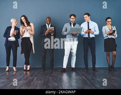 Theyve tutti hanno ottenuto i sensi astuti fare il commercio. Studio di un gruppo di uomini d'affari che utilizzano vari dispositivi digitali su uno sfondo grigio. Foto Stock