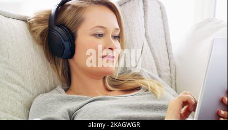 Adoro la navigazione tra diversi tipi di musica. Una giovane donna attraente che ascolta musica con le cuffie a casa. Foto Stock