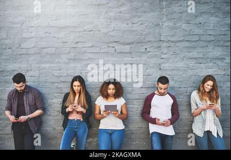 Tutti hanno il loro dispositivo preferito: Un gruppo di giovani che utilizzano i loro dispositivi wireless insieme all'esterno. Foto Stock