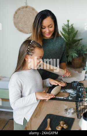 Mamma e la sua figlia di sei anni stanno facendo biscotti di Natale zenzero in cucina, stendendo l'impasto Foto Stock